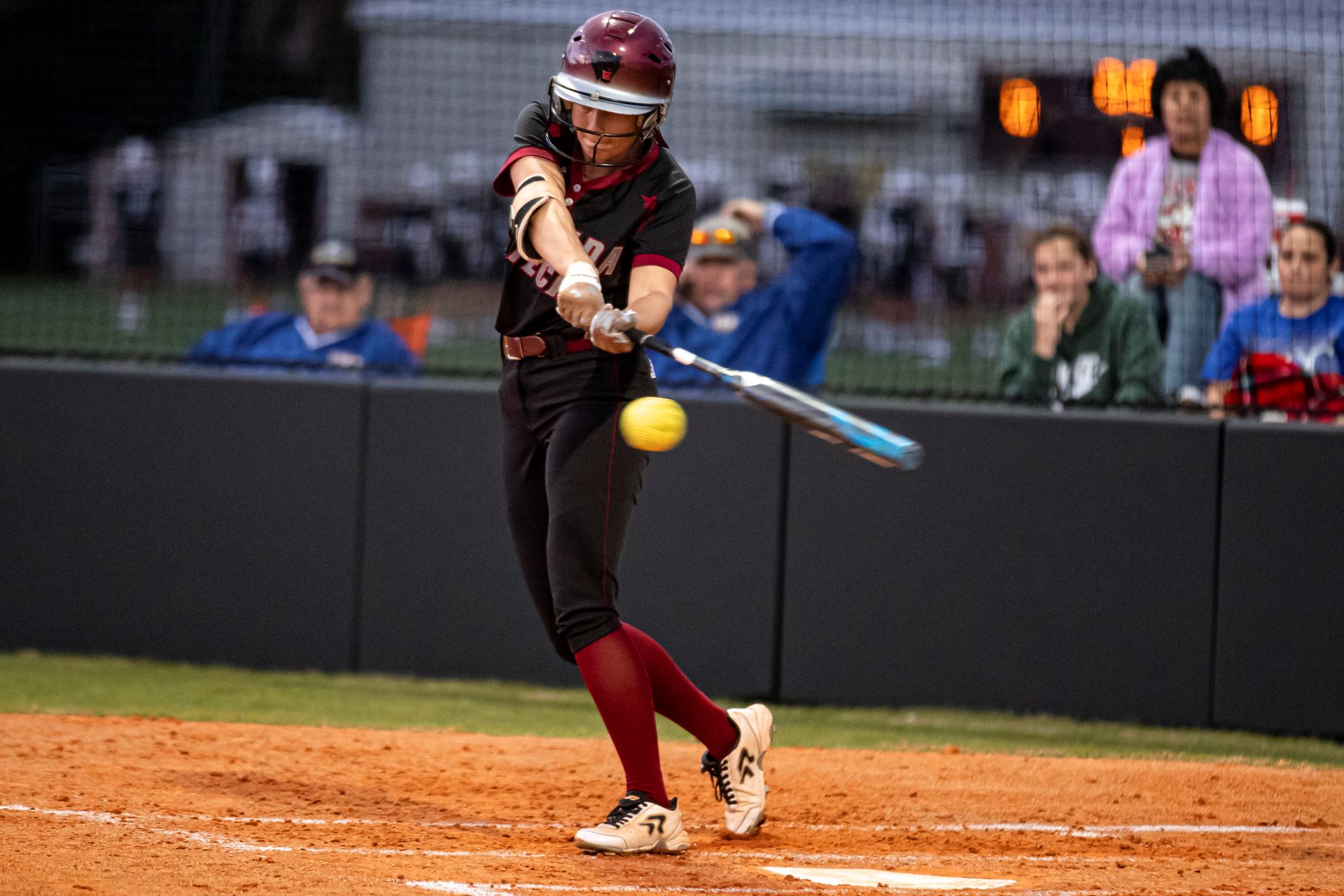 Florida Tech softball player swinging at a pitch, making contact with the ball, while spectators watch from behind the fence